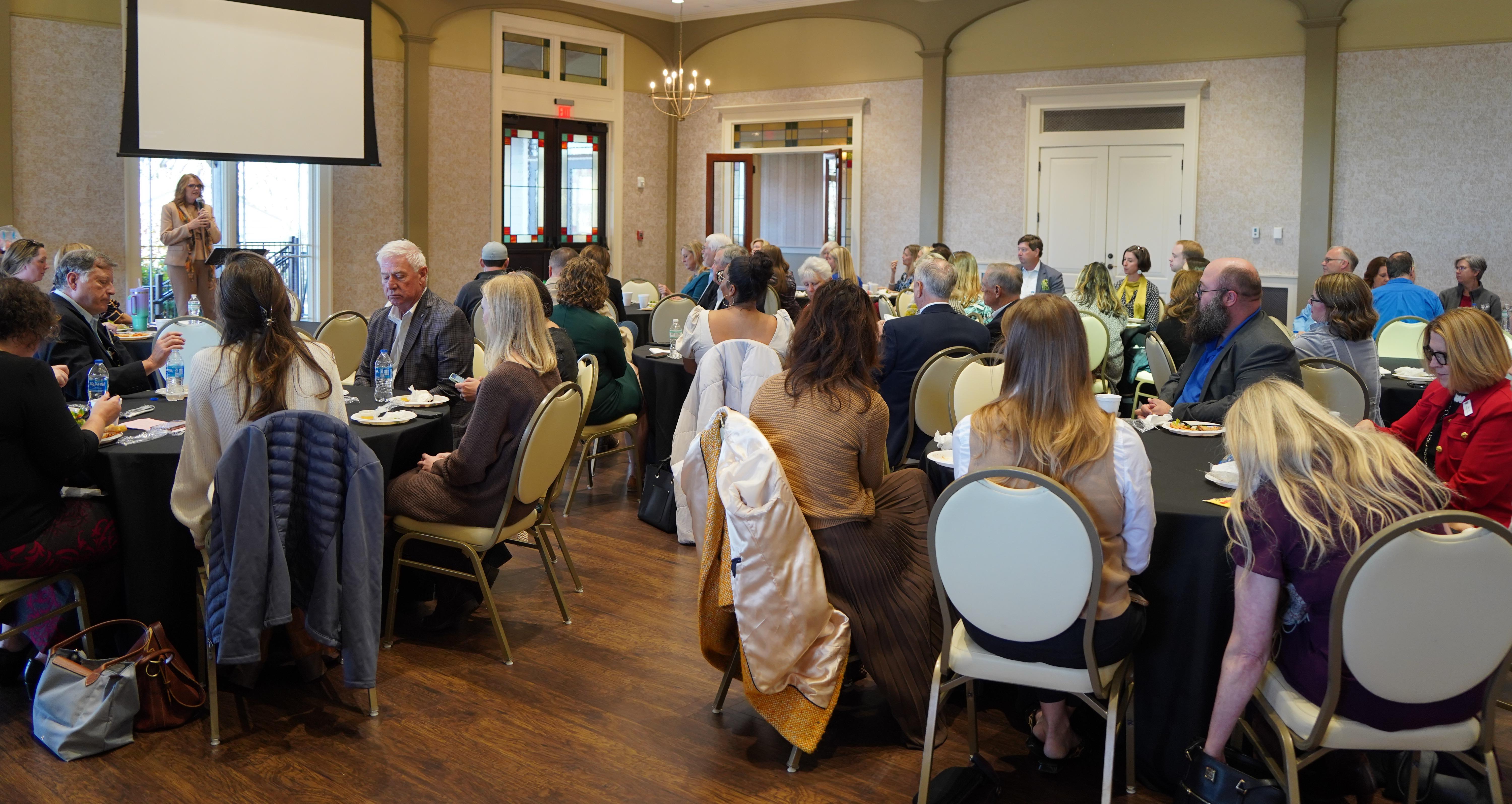 Speaker with microphone talking to seated room of people